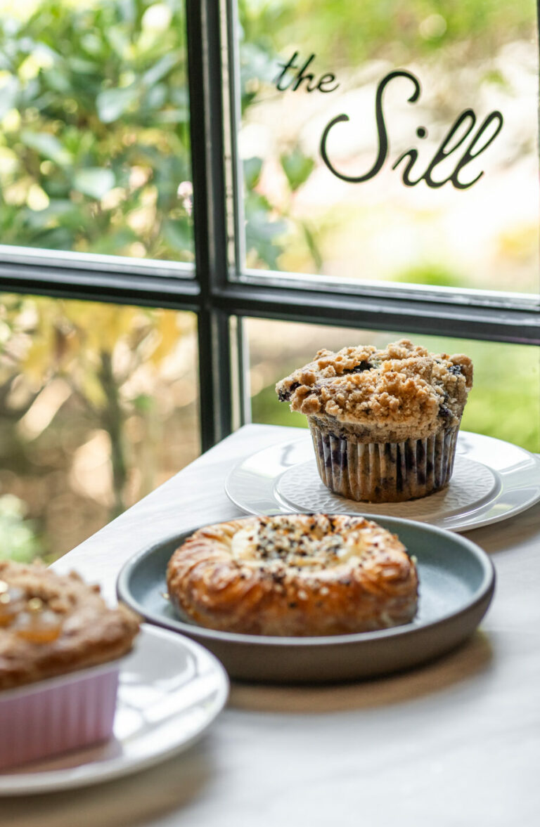 Three pastries sit on plates atop a table by a window with greenery and flowers outside; "the Sill" appears on the glass, evoking the relaxed atmosphere of a resort like Wequassett Resort & Golf Club.