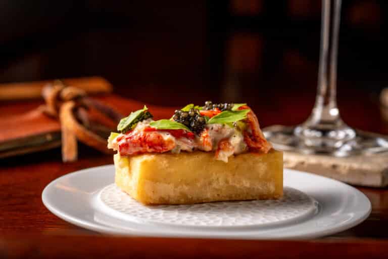 A gourmet appetizer with lobster, caviar, and fresh herbs on a rectangular piece of bread, served on a white plate.