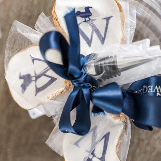 Three decorated cookies shaped like leaves with navy blue letters and images, tied together with tulle and a navy satin ribbon, placed on a clear surface.