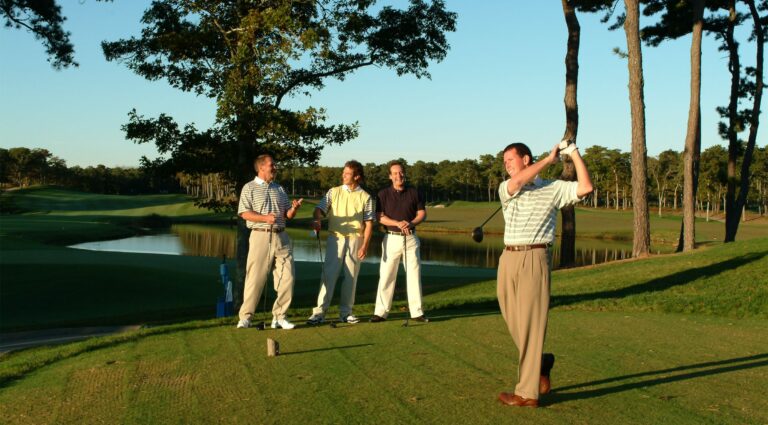 Man swinging a golf club while others watch at a Cape Cod golf course