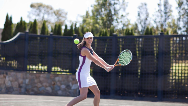 Smiling woman swings racquet at tennis ball
