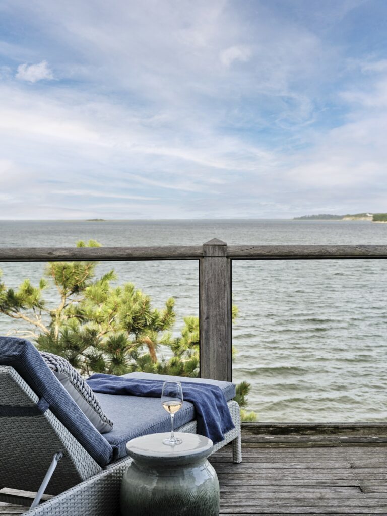 Scenic water view from a private balcony at Wequassett Resort, featuring outdoor dining furniture and a comfortable sitting area with patterned throw pillows.