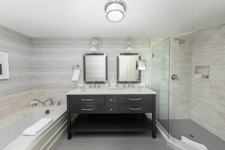 Modern bathroom in a Cape Cod hotel with a double-sink vanity, two mirrors, a glass-enclosed shower, and a bathtub with a white towel and toiletries—perfect for relaxing after celebrating at 28 Atlantic or your Cape Cod wedding venue.