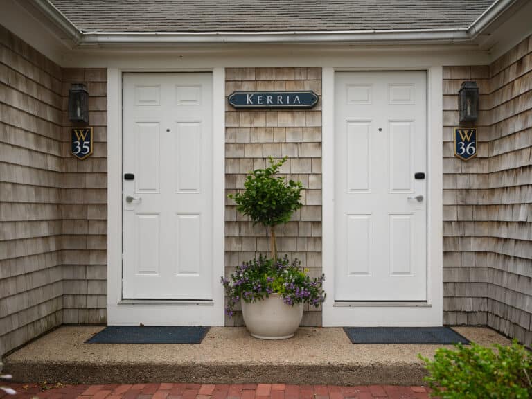 Two white doors labeled W35 and W36 on a shingled building with a "Kerria" sign above, separated by a potted plant with flowers—capturing the coastal charm of a Cape Cod hotel near Wequassett Resort and Golf Club.