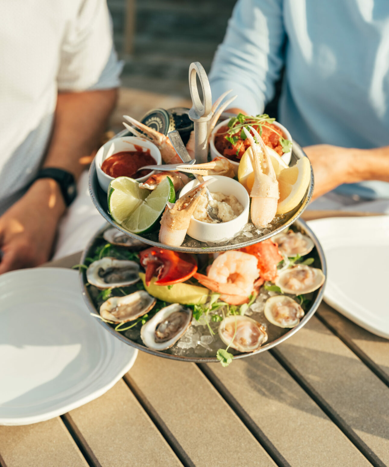 Two people sit at a table with a two-tiered seafood platter featuring oysters, shrimp, crab claws, lemon wedges, and dipping sauces at a charming Cape Cod hotel.