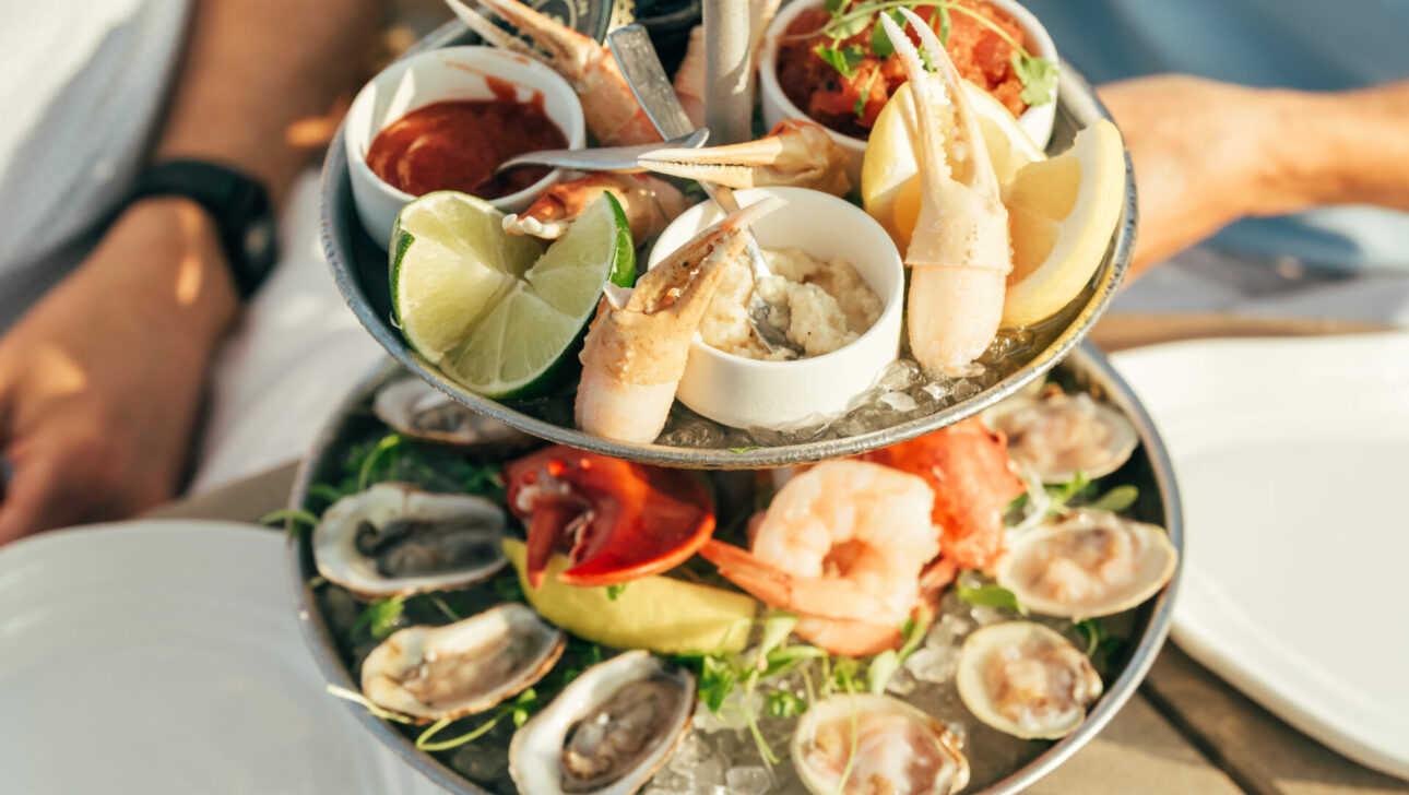 Two people sit at a table with a two-tiered seafood platter featuring oysters, shrimp, crab claws, lemon wedges, and dipping sauces at a charming Cape Cod hotel.