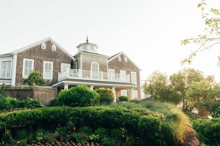 Two-story house with brown shingle siding, white trim, a central cupola, upper balcony, and a landscaped front yard—just minutes from Cape Cod golf course and the renowned Wequassett Resort and Golf Club.