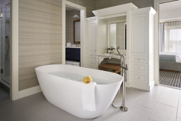 Modern bathroom with a freestanding white bathtub, towel and sponge on the edge, vanity area, and a glimpse of adjacent rooms—perfect for relaxing after a day at the Cape Cod golf course or exploring your favorite Cape Cod resort.