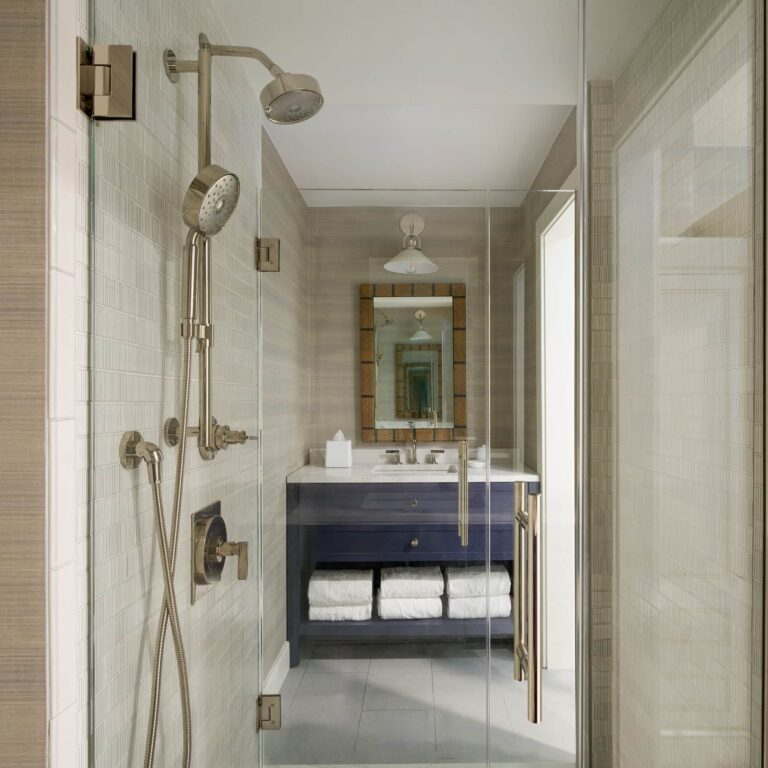 Modern bathroom at this Cape Cod hotel features a glass shower with dual showerheads, a vanity with a large mirror, and neatly stacked white towels—luxury details you'll find at Wequassett Resort and Golf Club.