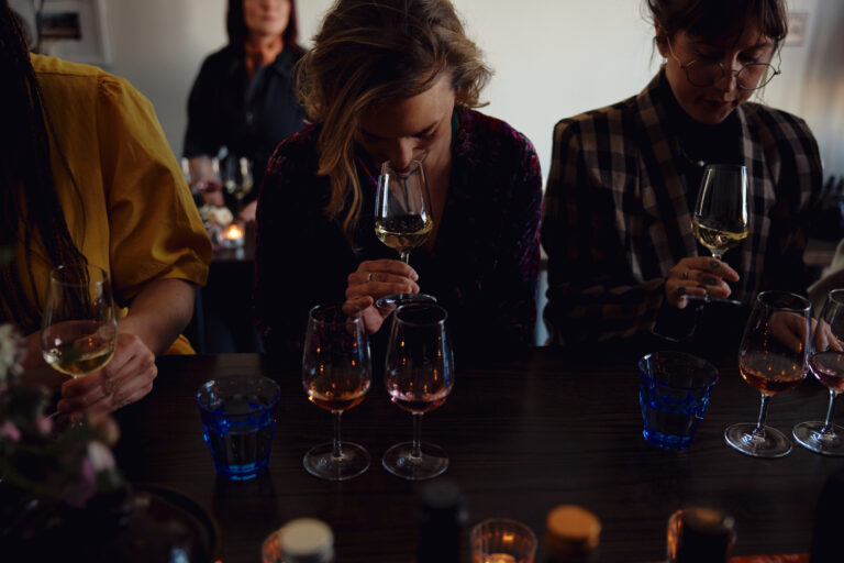 Three people seated at a table, each holding a wine glass during a Wine Dinner, with additional glasses of wine and water in front of them, possibly featuring selections from Silver Oak Cellars.