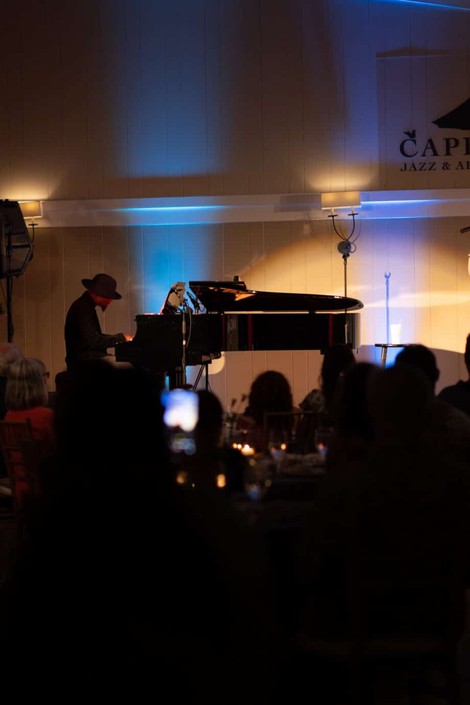 A singer performs on stage with a pianist at the Cape Cod Jazz & Arts Festival during Wequassett evenings, while an audience watches in a dimly lit venue.