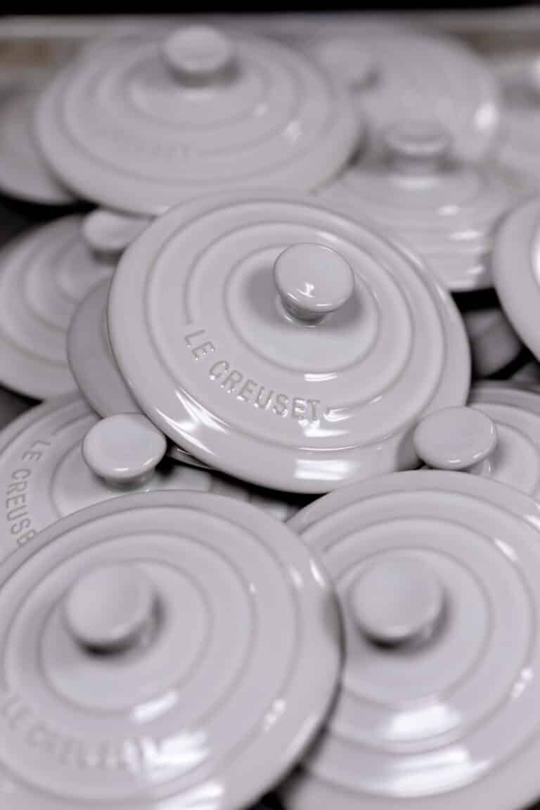 A pile of overlapping white Le Creuset pot lids, all with round knobs and the brand name embossed on each lid, evokes the charm of Supper on the Bay.