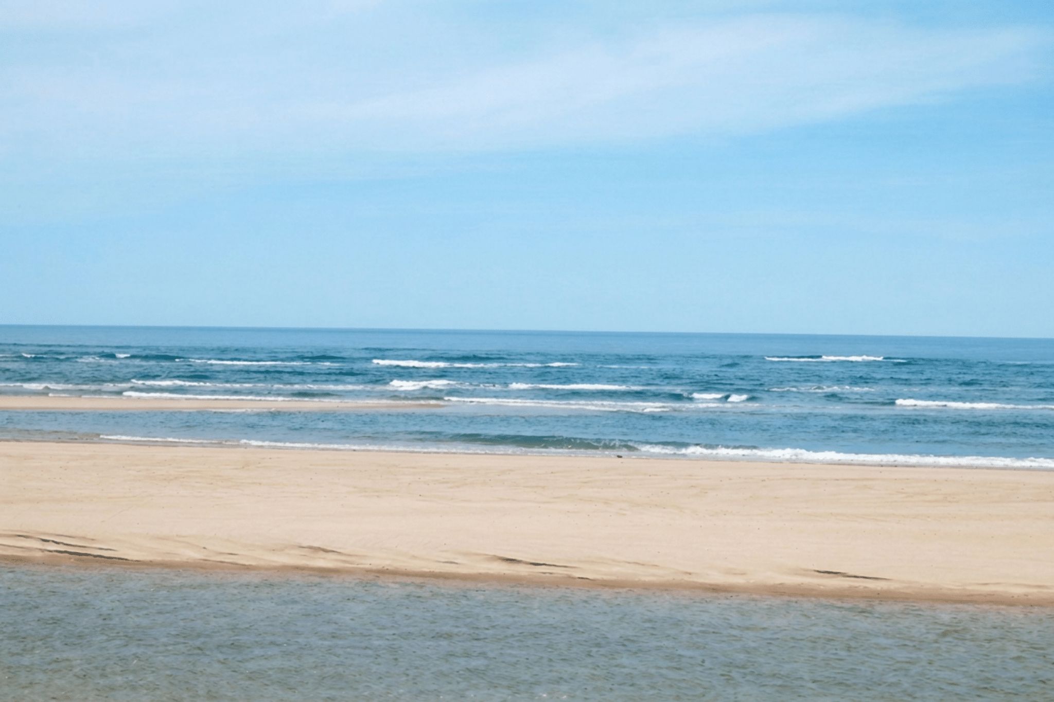 A sandy beach with gentle waves and a clear blue sky on a bright day invites you to begin your Journey to the Outer Beach.