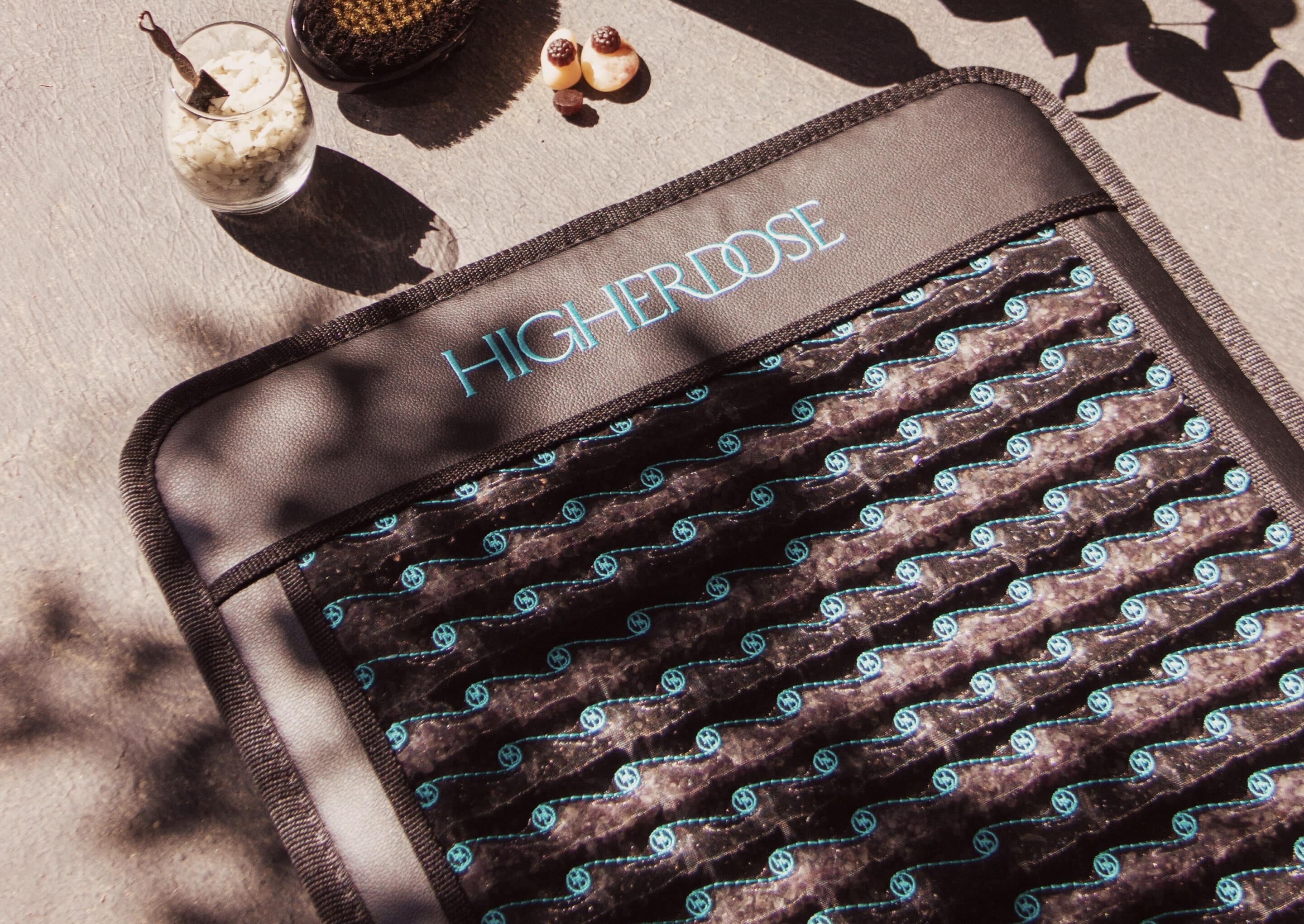 A rectangular mat labeled "HIGHERDOSE" lies on a gray surface next to a glass of oats, two small pastries, and a jar with a straw.