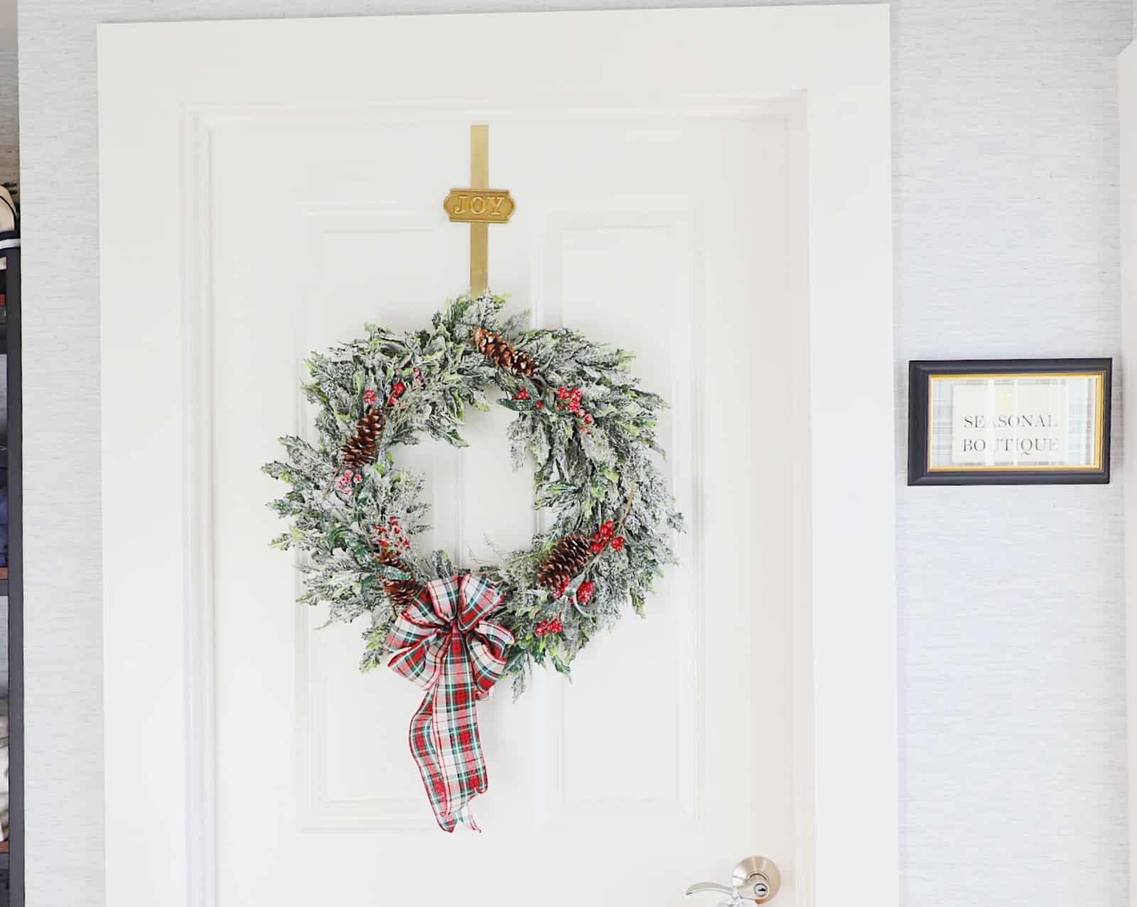 A white door decorated with a green wreath featuring a plaid bow and silver jingle bells hanging from the handle creates a true seasonal masterpiece.