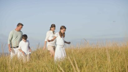Family of four walking through a field of tall grass.