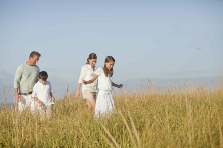 Family of four walking through a field of tall grass.