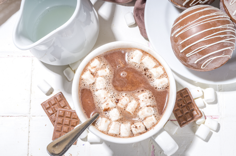 Hot chocolate with marshmellows sitting on a table with treats.