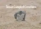 A grey, weathered stone sits in the sand at the Merry Market, with the text “Susan Campbell Creations” overlaid above it.