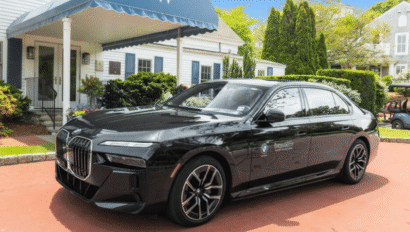 A black BMW sedan is parked on a red brick driveway in front of a white building with blue shutters and a canopy labeled with a "W," evoking the classic elegance of Wequassett Resort & Golf Club.