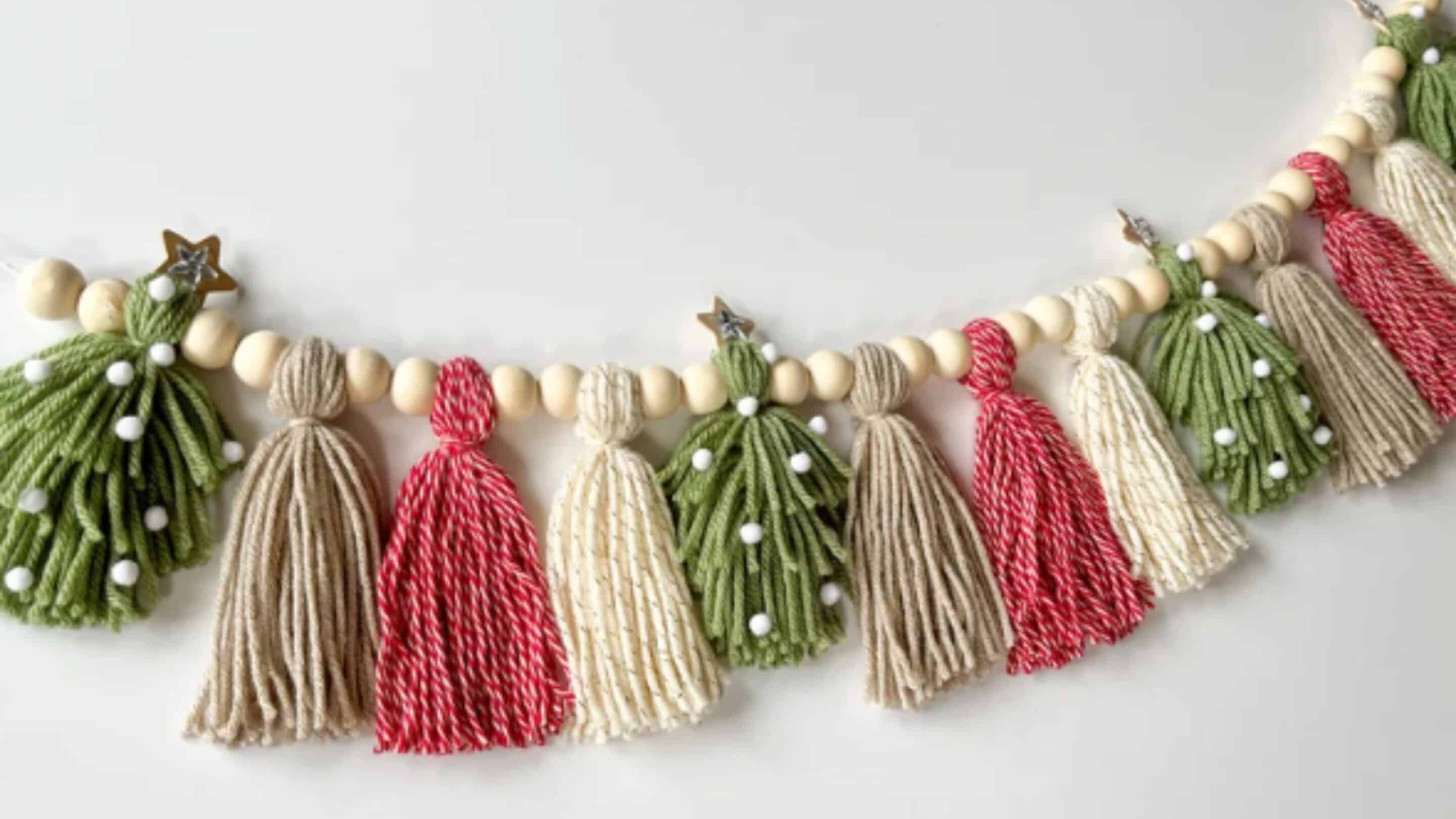 A decorative garland from our Garland Workshop, featuring wooden beads, yarn tassels in red, cream, and green, plus green yarn Christmas trees adorned with white pom-poms and gold star toppers—perfect for adding Nature’s Elegance to your holiday décor.