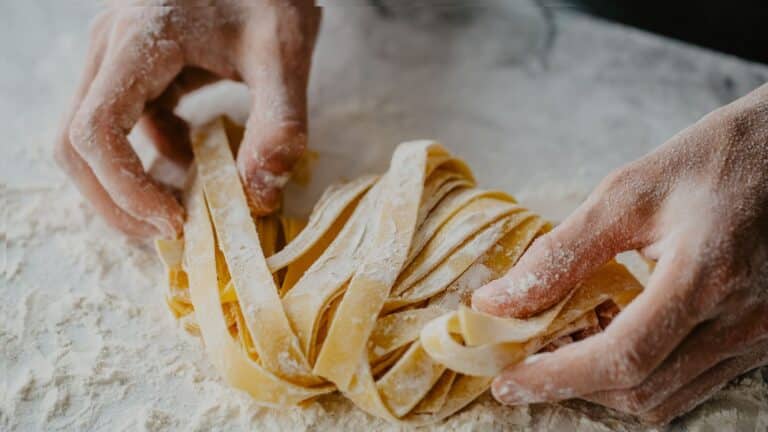 Hands dusted with flour arrange fresh, uncooked pasta noodles on a floured surface—a classic scene from hands-on cooking classes or culinary school chef training.