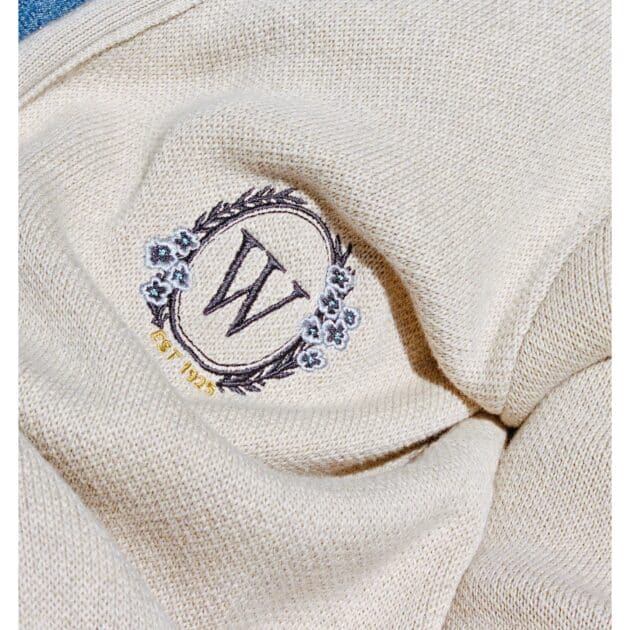Close-up of beige fabric featuring an embroidered "W" inside a floral wreath, with "EST 1995" in yellow text below—a nod to our exclusive NY collaboration.