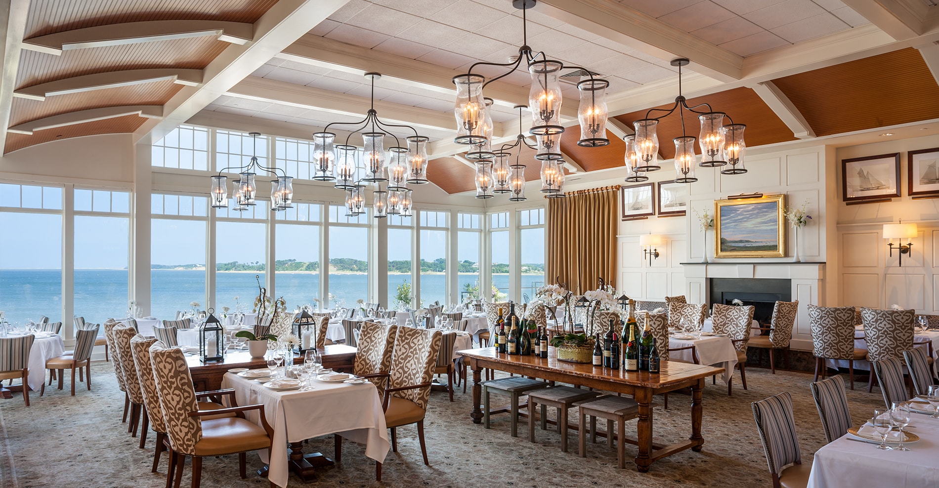 Elegant restaurant dining room with large windows overlooking a waterfront view, set tables featuring Atlantic Menus, patterned chairs, and decorative lighting fixtures.