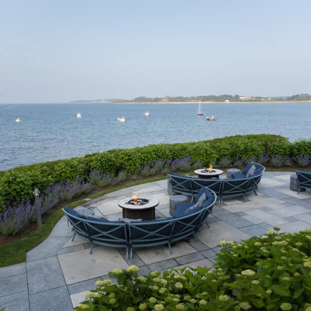 A patio with chairs and a fire pit overlooking a body of water.