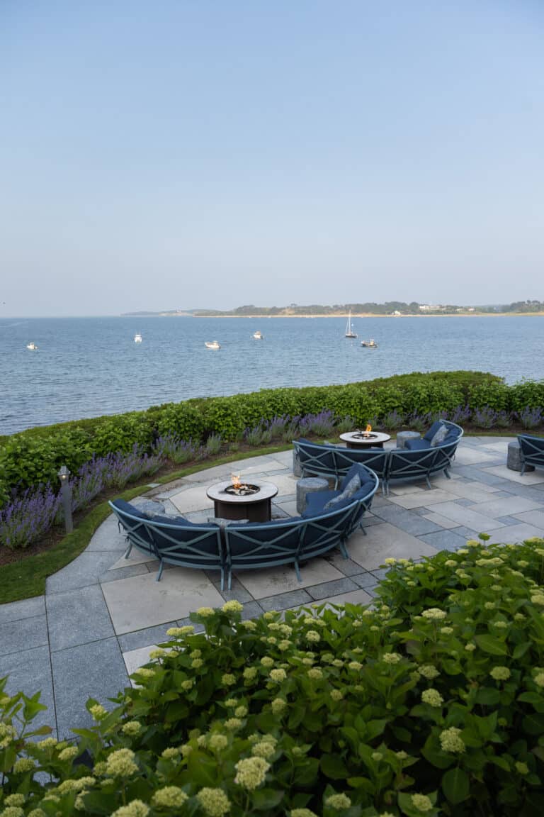 A patio with chairs and a fire pit overlooking a body of water.