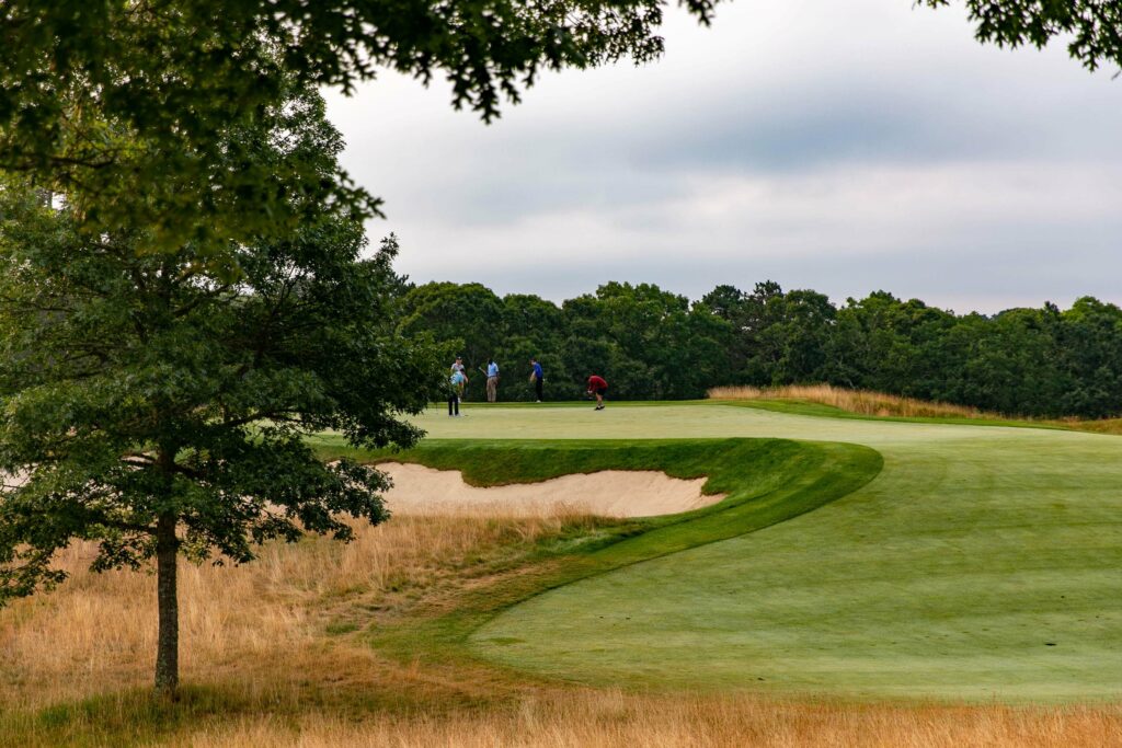 Four people stand on a green at a golf course, with trees and sand bunkers nearby under a cloudy sky—perfect for enjoying the game or exploring special offers on memberships and events.