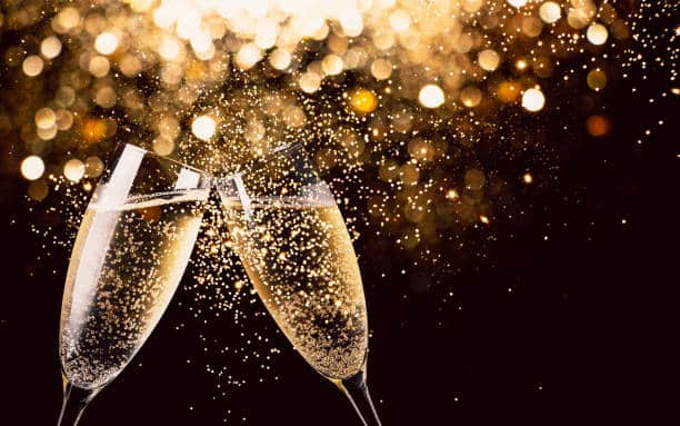 Two champagne glasses clinking with bubbles rising, set against a dark background with golden bokeh lights—perfect for celebrating a magical New Year's Eve event at Wequassett.