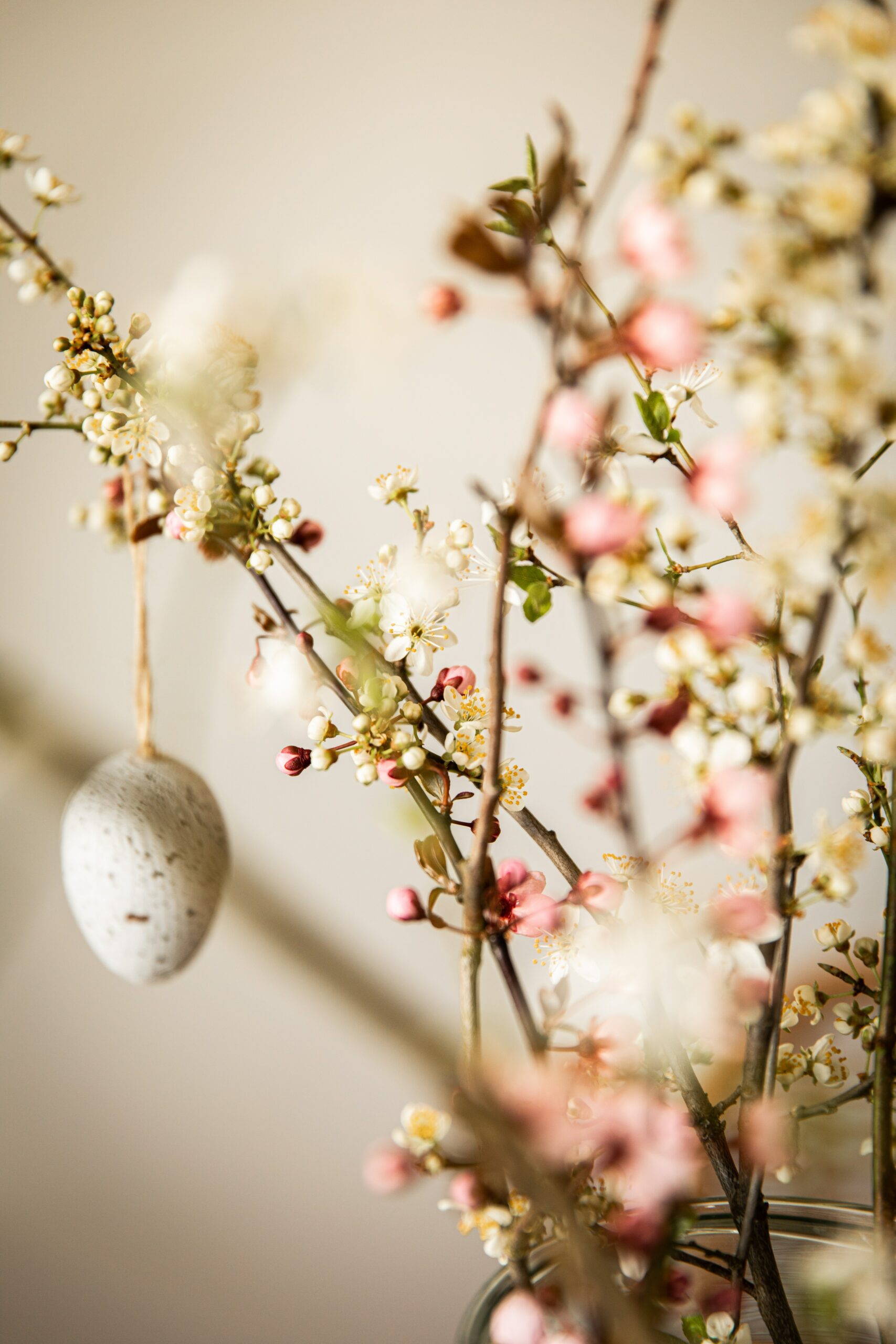 Branches with white and pink blossoms are arranged in a vase, with a speckled egg ornament hanging from one branch—a charming centerpiece perfect for Easter celebrations or springtime at Wequassett.
